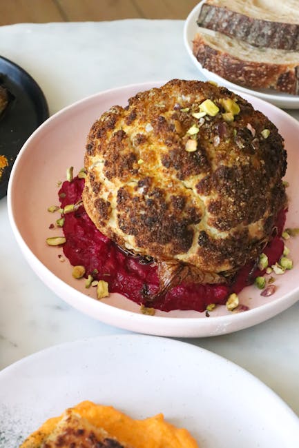 From above of whole roasted cauliflower on creamy beetroot sauce served on table with fresh bread in restaurant